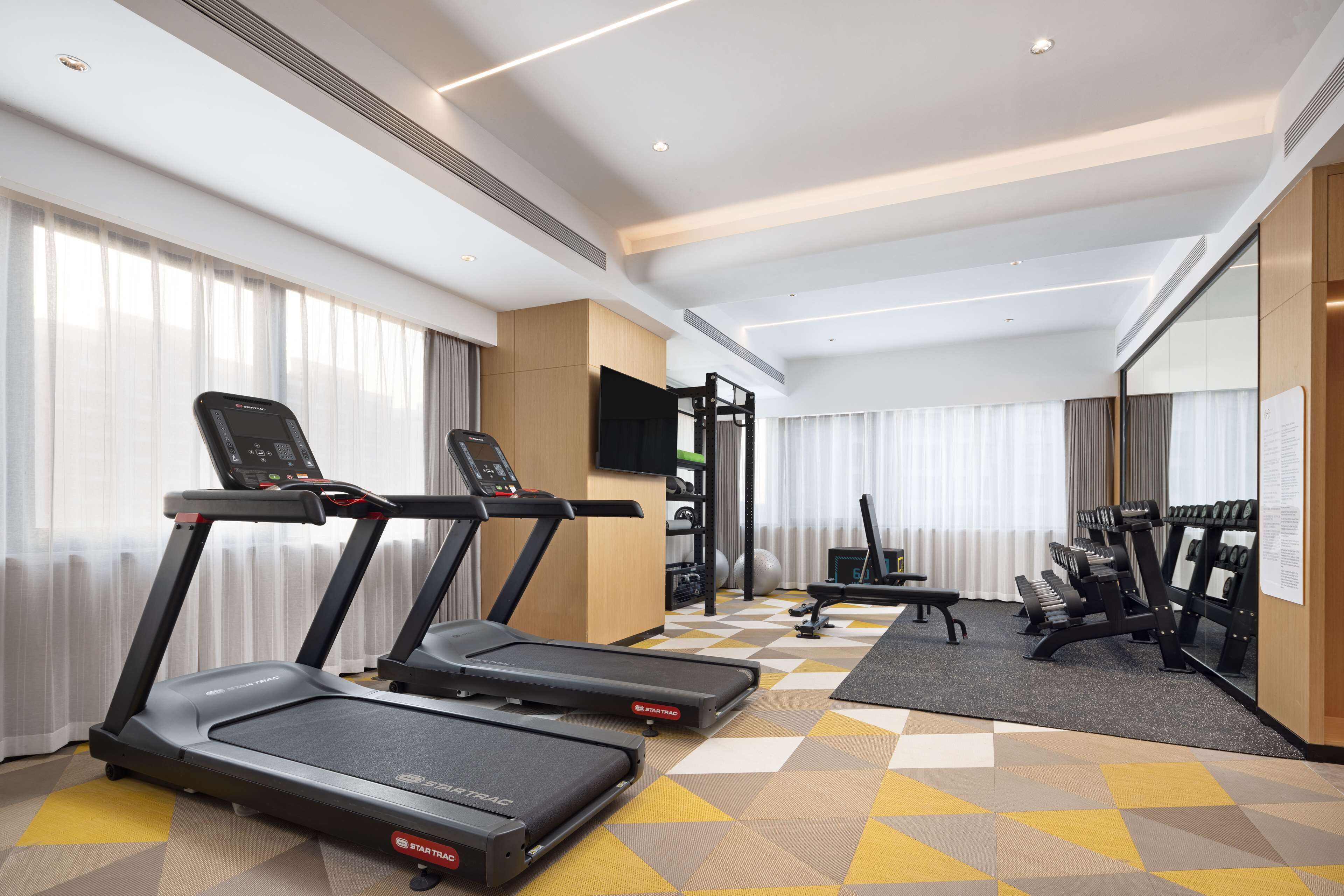 A hotel fitness room with treadmills, a bench, and weight equipment.