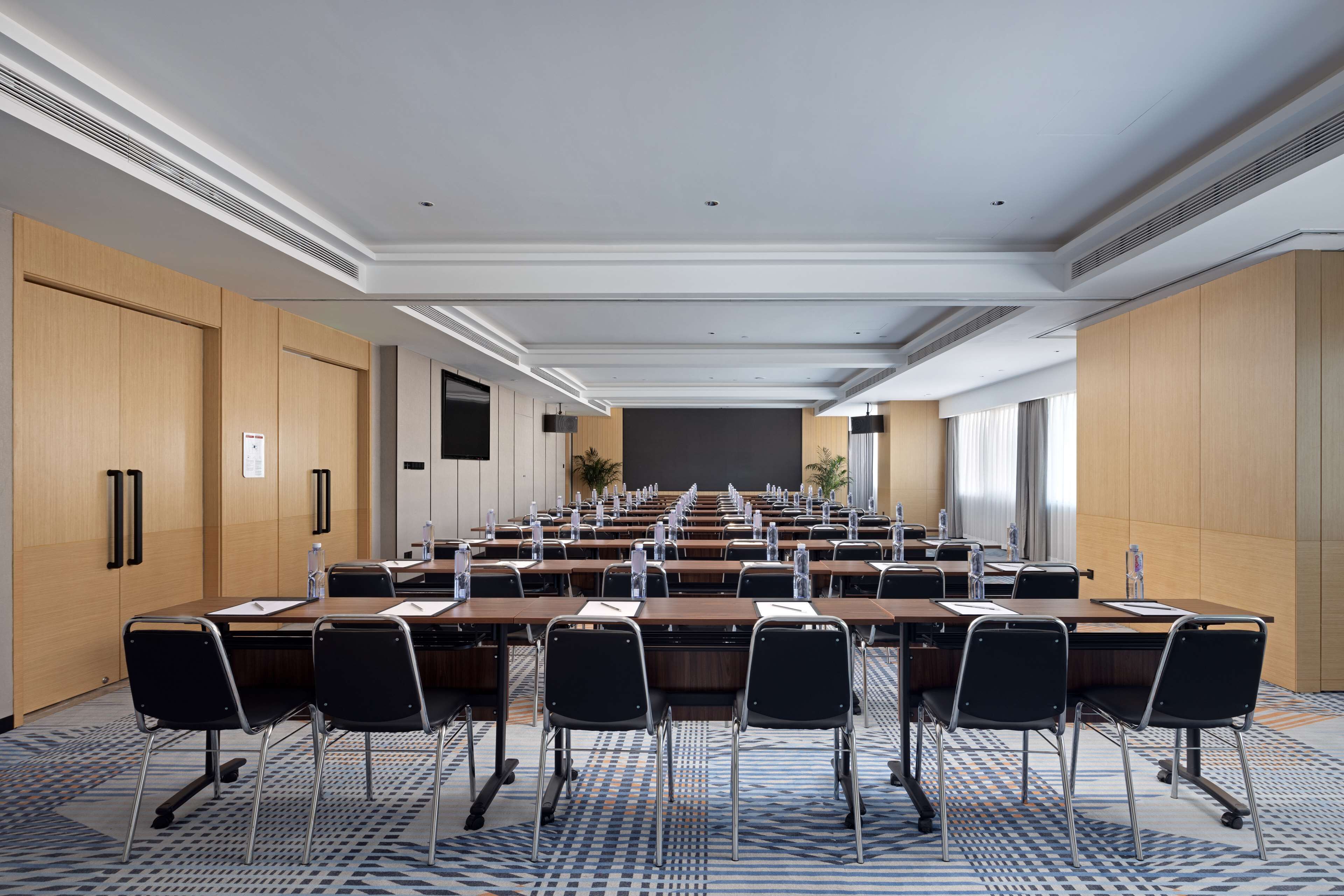 A conference room with a long table, multiple chairs, and a projector screen at the front.