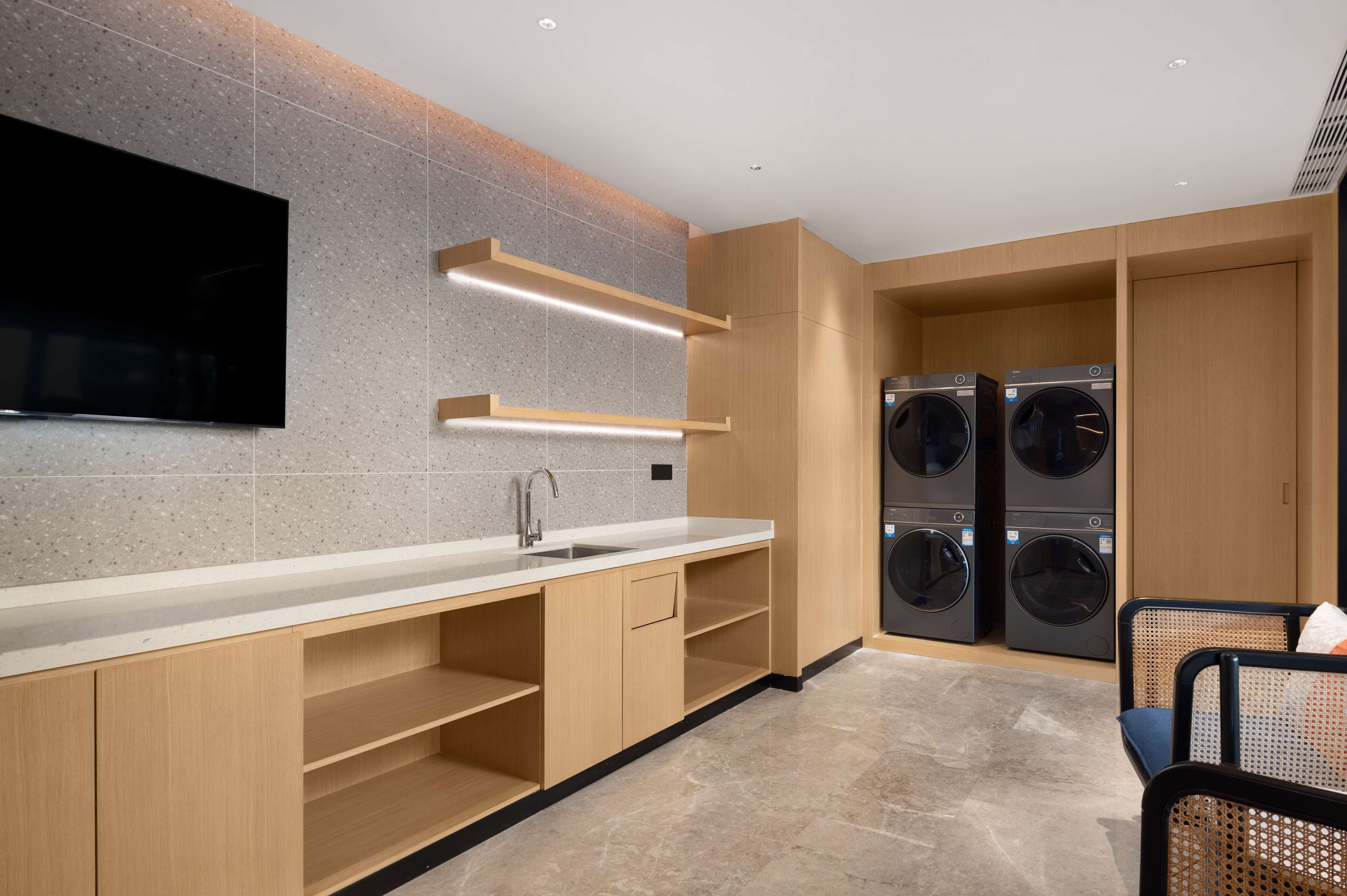 A modern kitchen with a flat-screen TV, built-in washing machines, and wooden cabinetry.