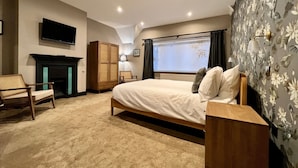 Un dormitorio con cama, televisor, chimenea, armario y ventana con cortinas.