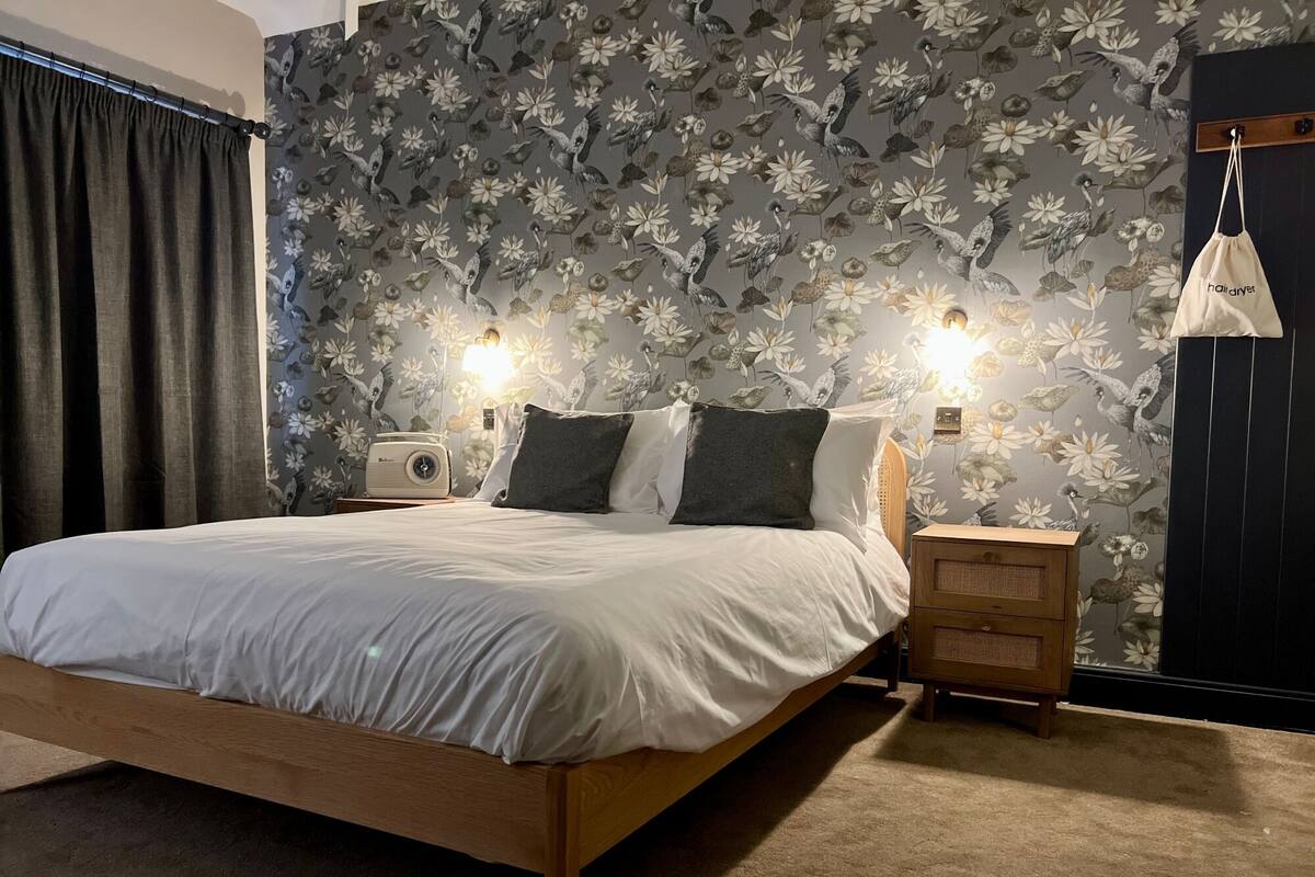 A bedroom with a wooden bed, a nightstand with a lamp, and a floral wallpaper.