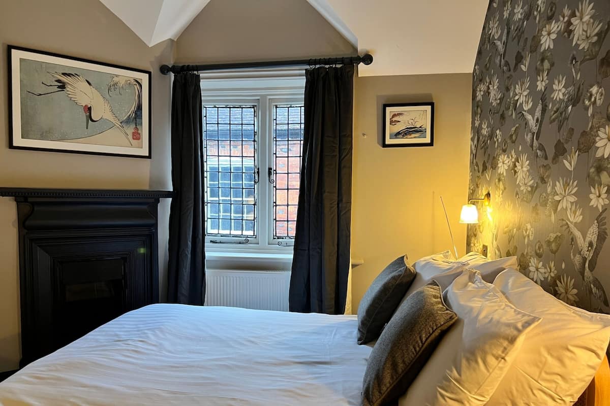 A bedroom with a large bed, a fireplace, and a window with curtains.