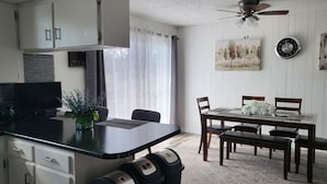 Una cocina moderna con armarios blancos, encimera negra y un comedor con mesa y sillas de madera.