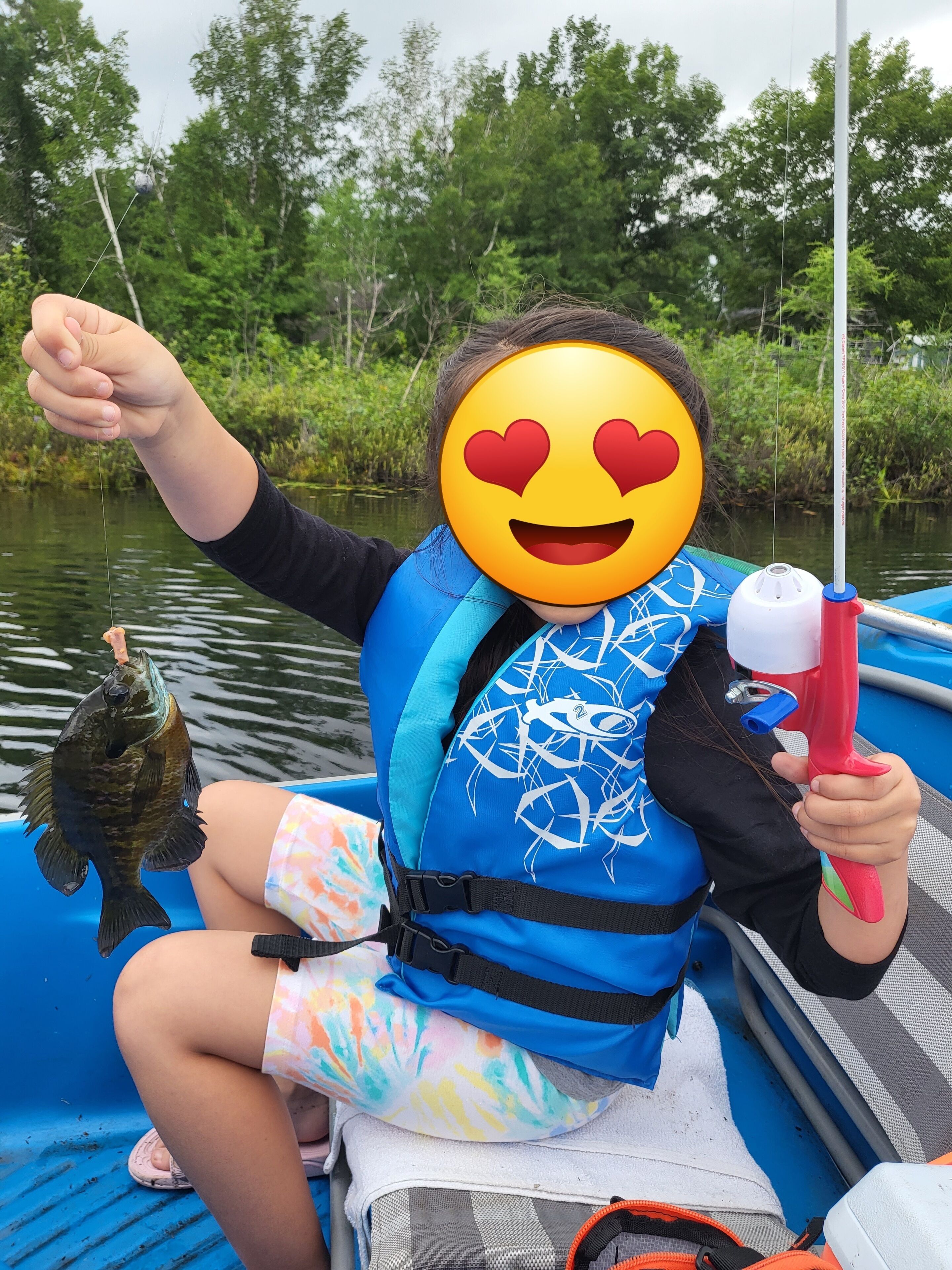 A person on a boat holding a fish, wearing a blue life jacket, and a heart-eyed emoji.