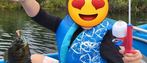 A person on a boat holding a fish, wearing a blue life jacket, and a heart-eyed emoji.