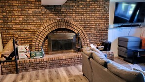Una sala de estar con chimenea de ladrillo, un televisor montado en la pared y un sofá seccional.