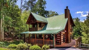A rustic cabin with a green metal roof, wooden exterior, and a porch with a railing. - Epic Retreat I Pickleball I Basketball I Arcade I Putting Green I Air Hockey (Sevierville)