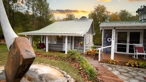 A rustic cabin with a porch, a small garden with autumn foliage, and a target on the door. - Lumberjack Family Retreat I Putt Putt I Pool Table I Darts I Hot Tub I Firepit (Sevierville)