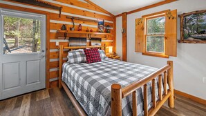 A wooden cabin bedroom with a bed, a window, a door, and a shelf with various items. - Lumberjack Family Retreat I Putt Putt I Pool Table I Darts I Hot Tub I Firepit (Sevierville)