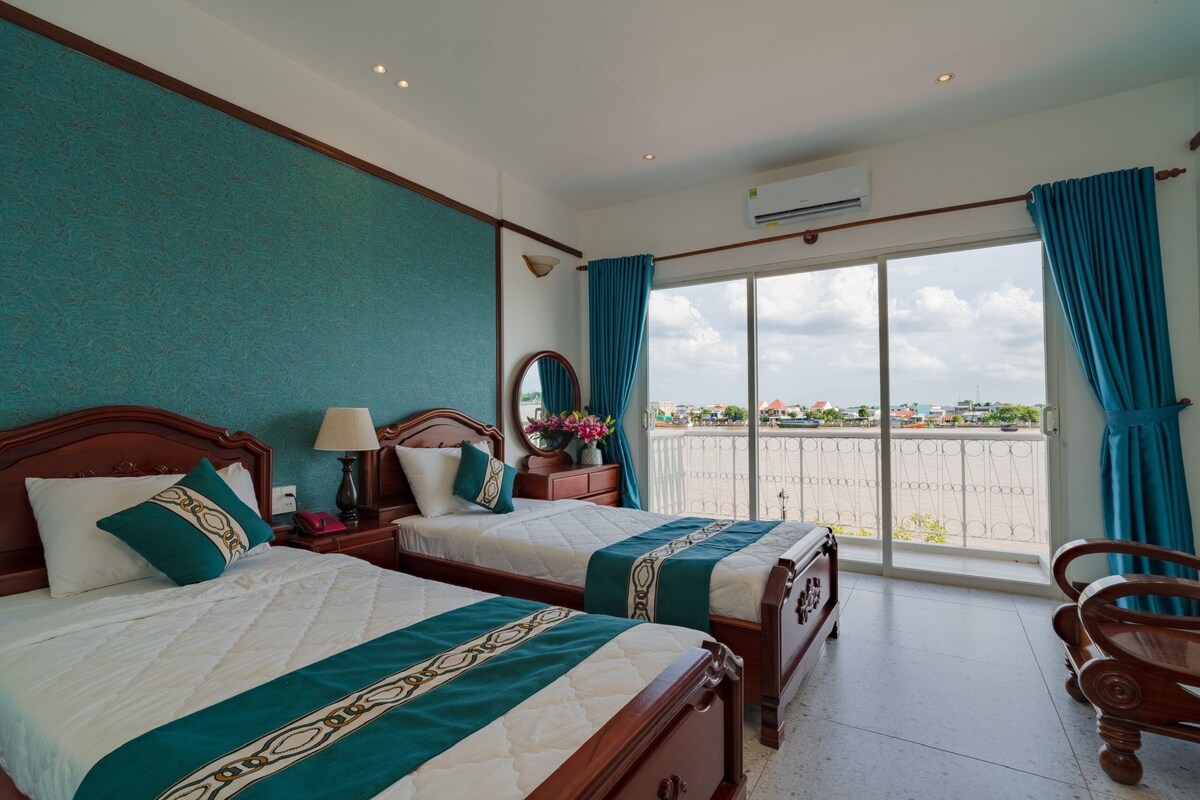 A hotel room with two beds, a balcony with a view, and a wooden chair.