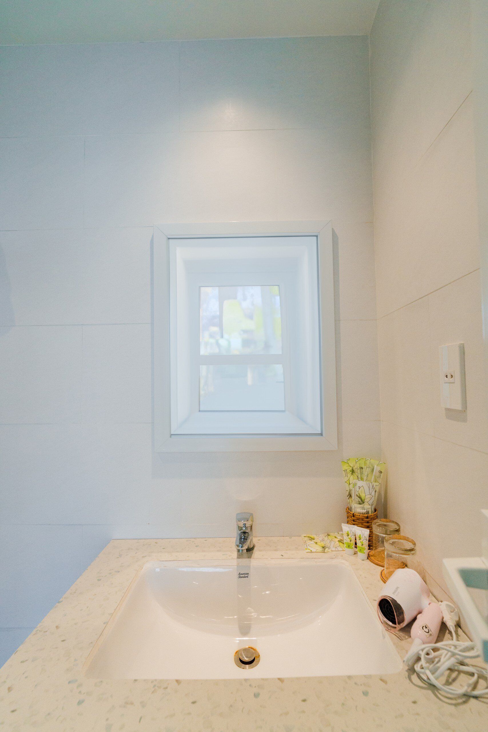 A bathroom with a white sink, a window above the sink, and a mirror.