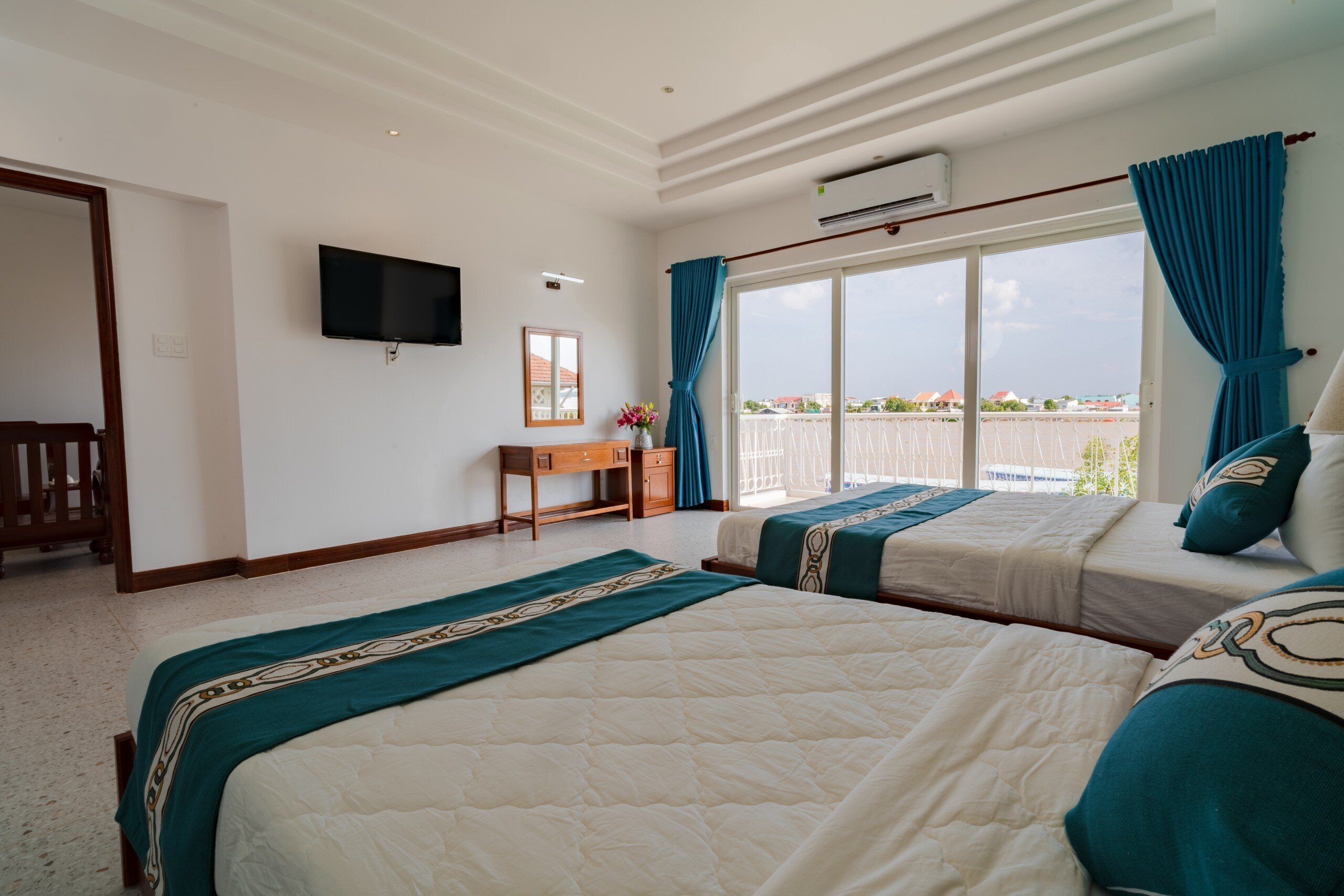A hotel room with two beds, a desk, a TV, and a balcony with a view.