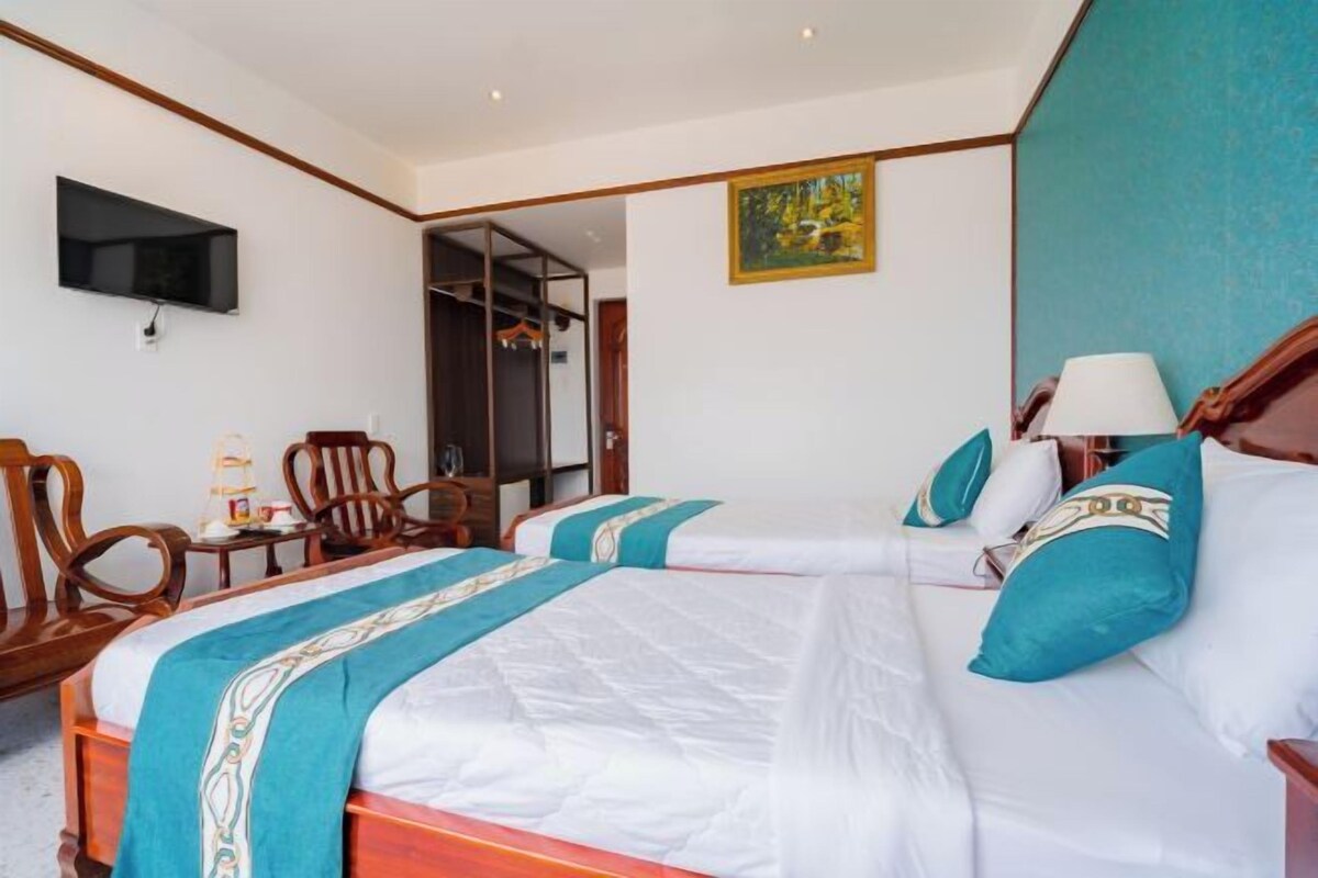 A hotel room with two beds, a TV, wooden furniture, and a painting on the wall.