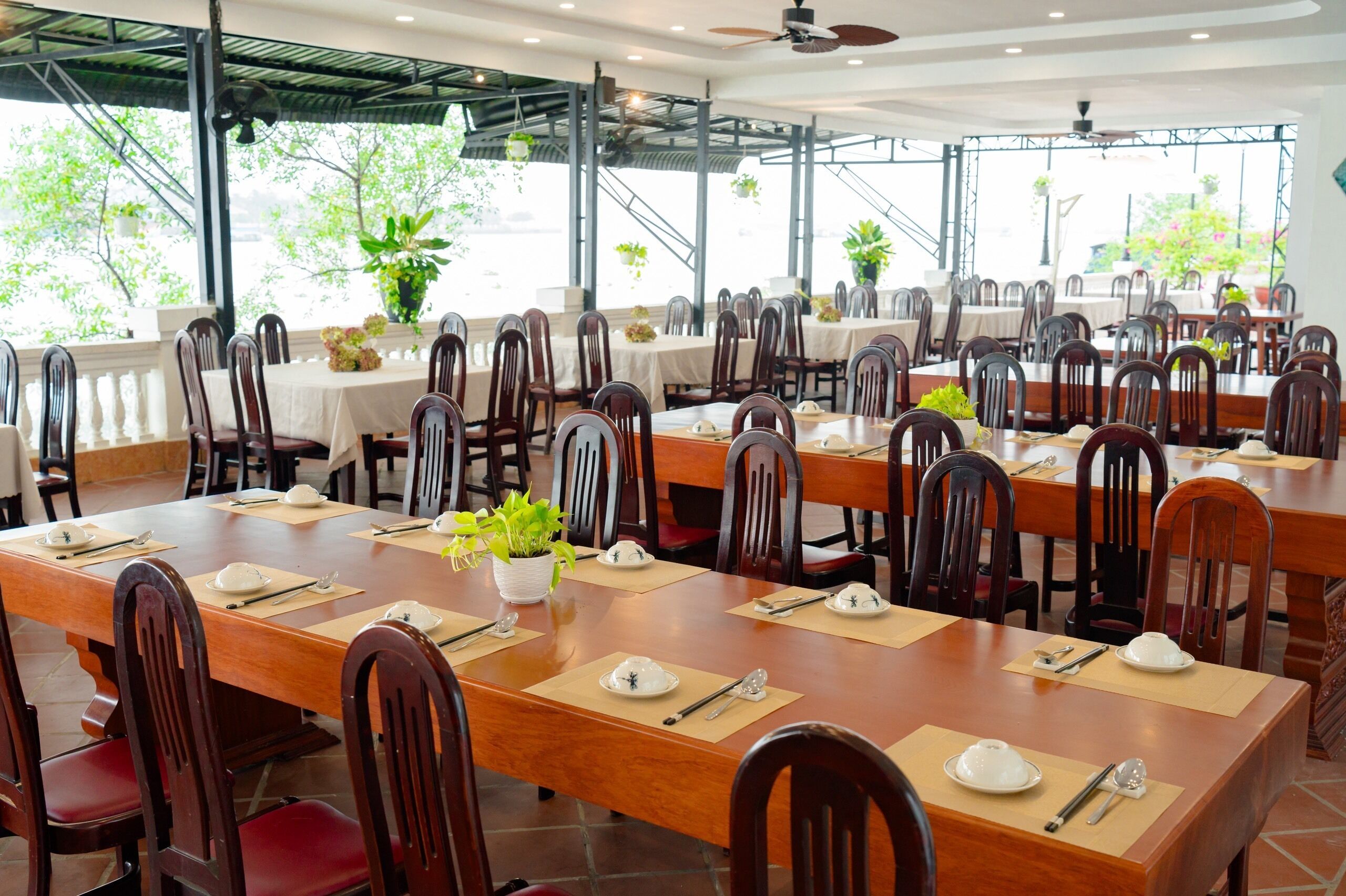 A restaurant with multiple tables set for dining, each with place settings and potted plants.
