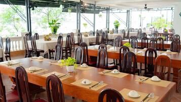 A restaurant with multiple tables set for dining, each with place settings and potted plants.