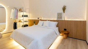 Ein modernes Schlafzimmer mit einem Bett, einem Holzkopfende, einem Nachttisch und einem an der Wand befestigten Regal mit Kleidung.