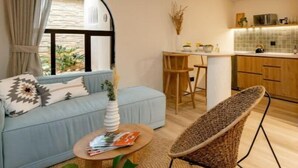 Ein modernes Wohnzimmer mit einer Couch, einem Couchtisch und einem Korbstuhl. Es gibt eine Küchenzeile mit einem Esstisch und Stühlen.