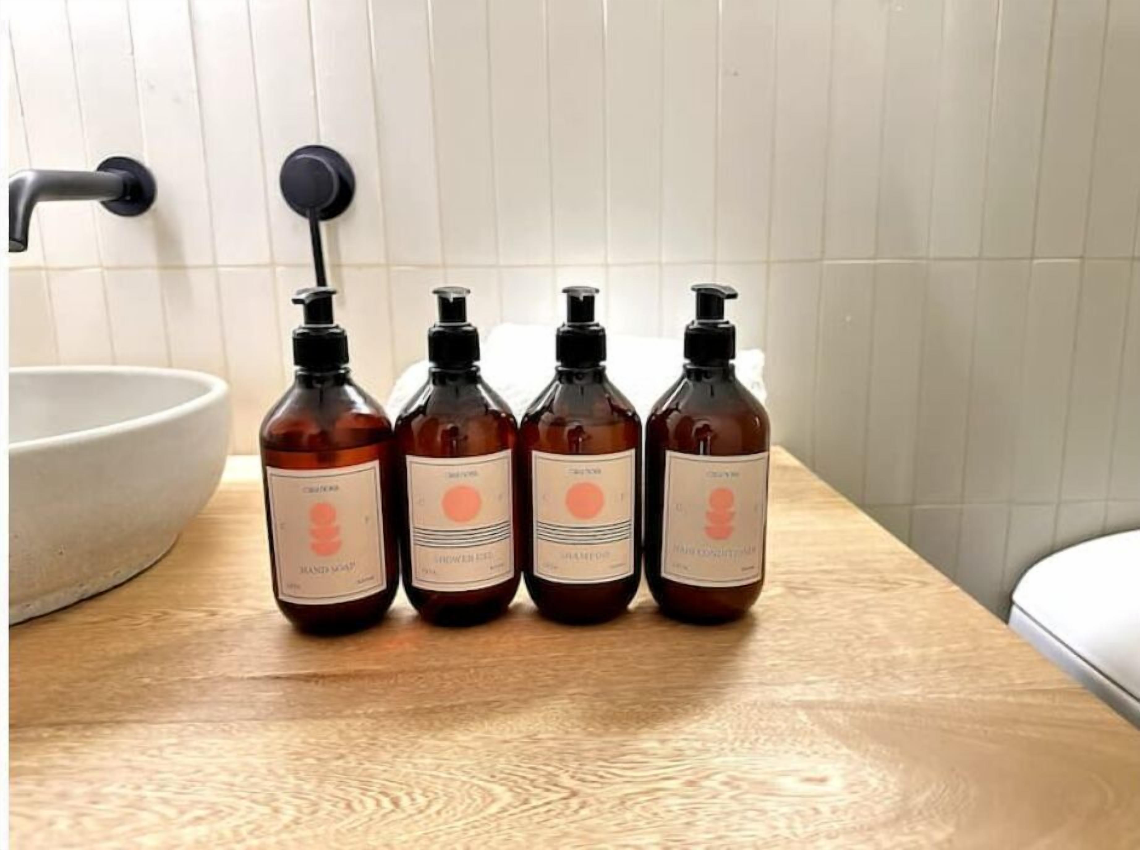 Cuatro botellas de productos para el cabello sobre una superficie de madera en un baño con un lavabo blanco y un grifo negro.