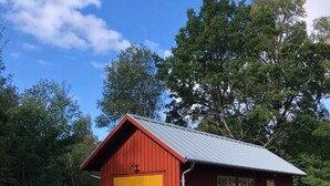 Ein rotes Gebäude mit einer gelben Garagentür, umgeben von Bäumen und einer Rasenfläche.