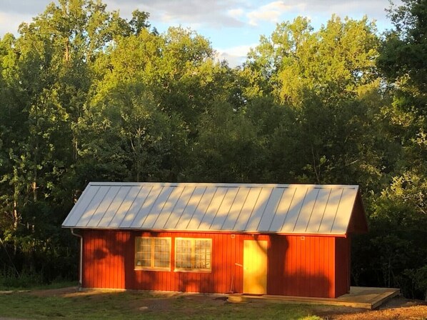 A small, single-story building with a sloped metal roof, surrounded by dense trees.