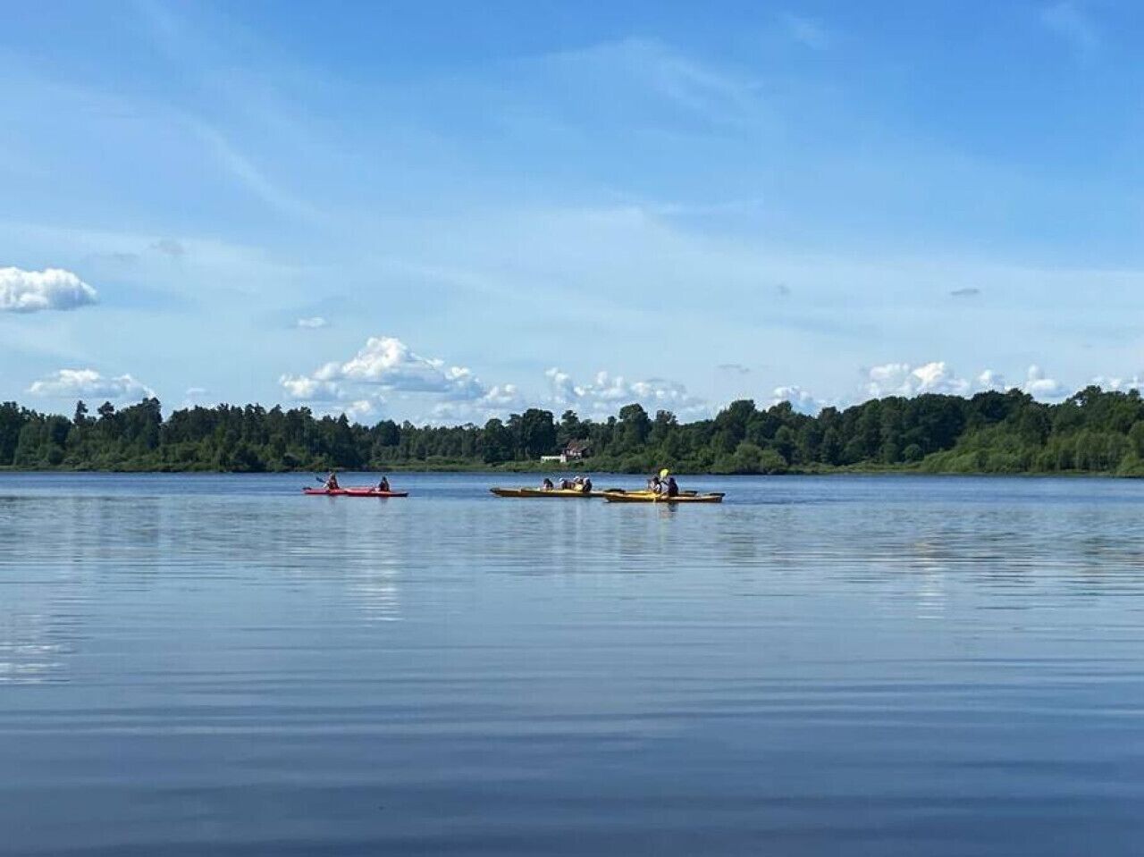 Ein ruhiger See mit Kajaks und Kanus, umgeben von Bäumen und einem klaren Himmel.