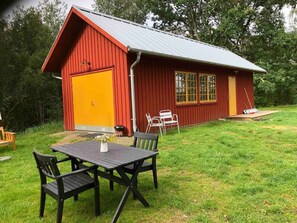 A red barn with a yellow door, a table with chairs, and a small garden area.