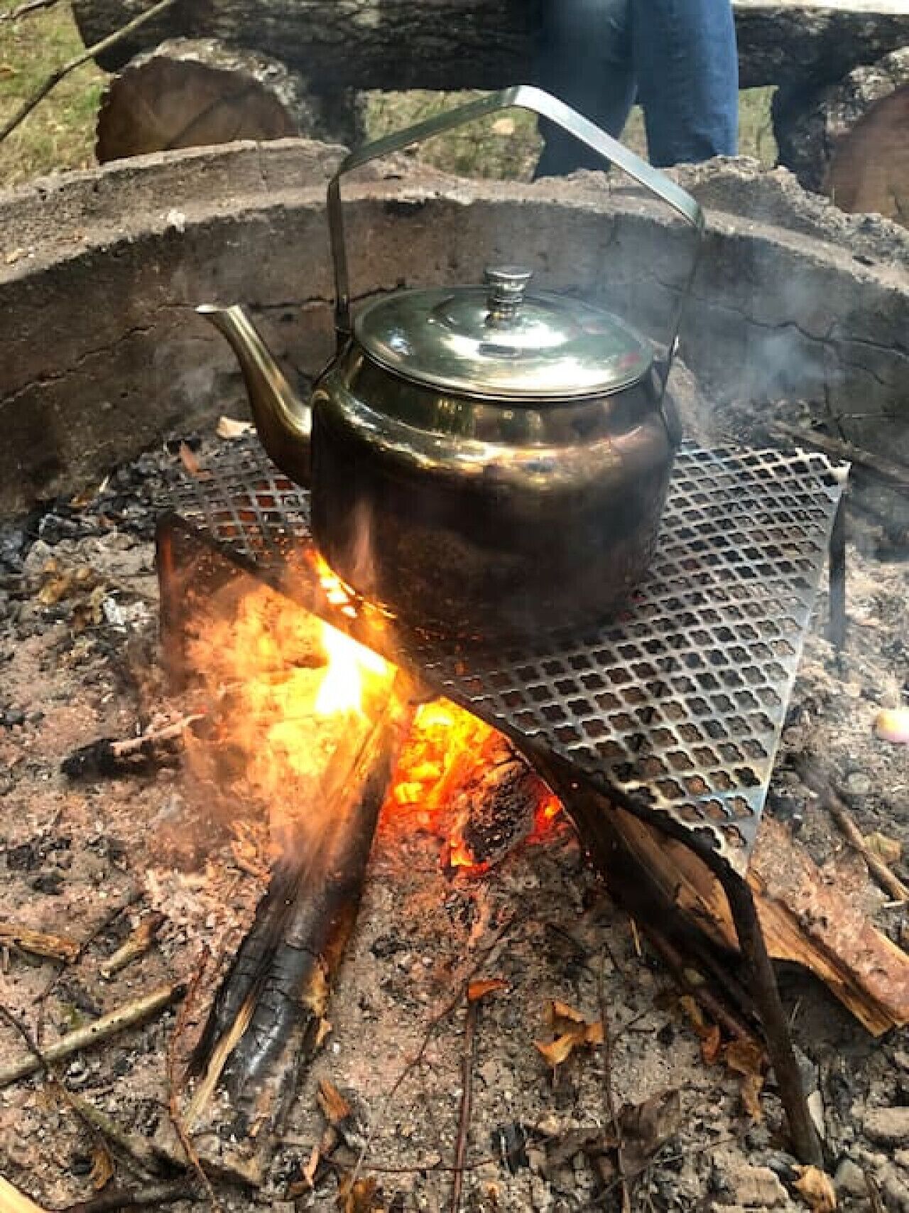 Une marmite en métal, posée sur une grille métallique au-dessus d’un feu de camp.