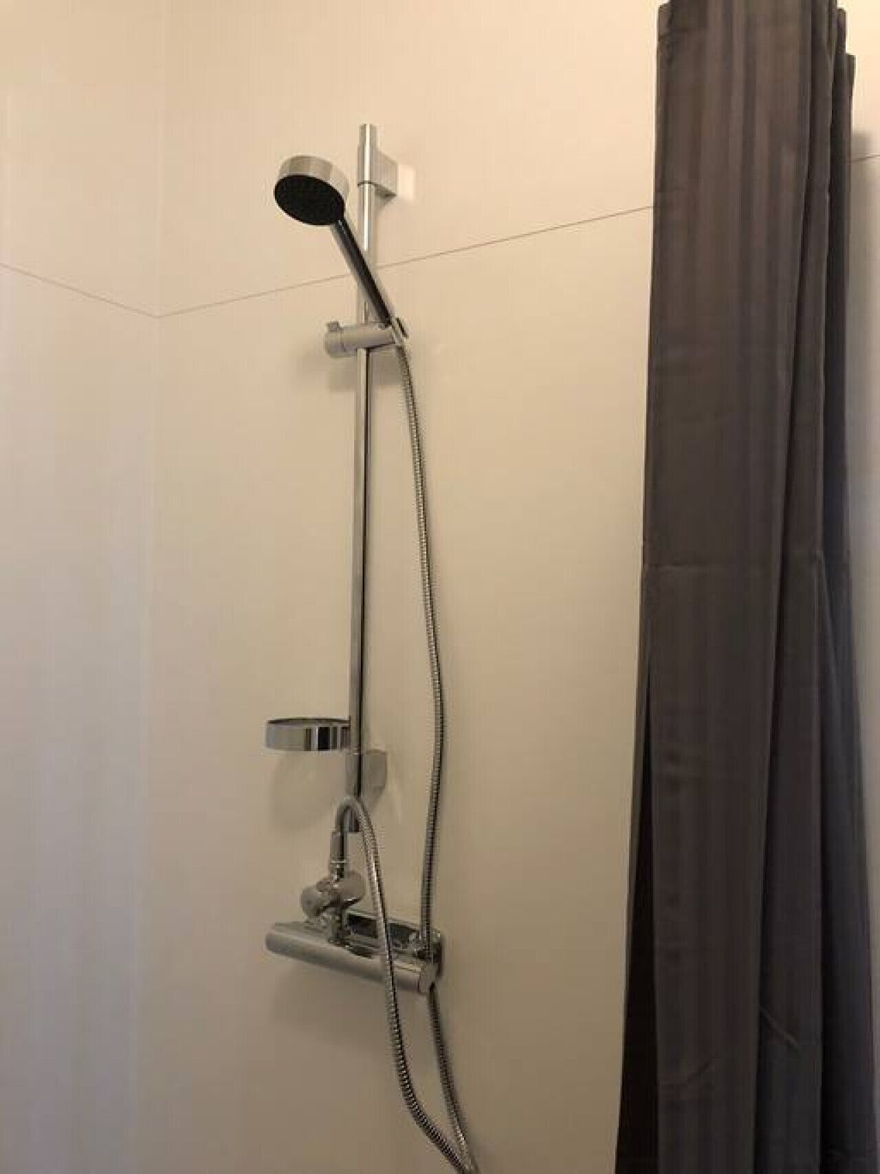 A shower with a handheld showerhead, a wall-mounted control panel, and a curtain.
