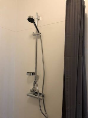 A shower with a handheld showerhead, a wall-mounted control panel, and a curtain.