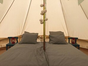 A tent with a bed, pillows, and two lanterns on nightstands.