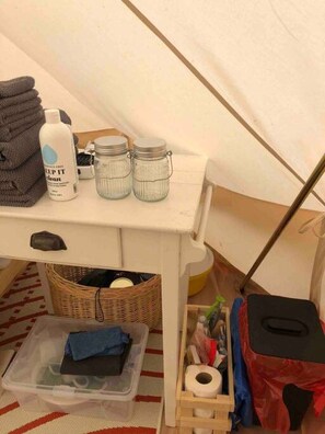 A white storage unit with a bottle, jars, and a folded towel.