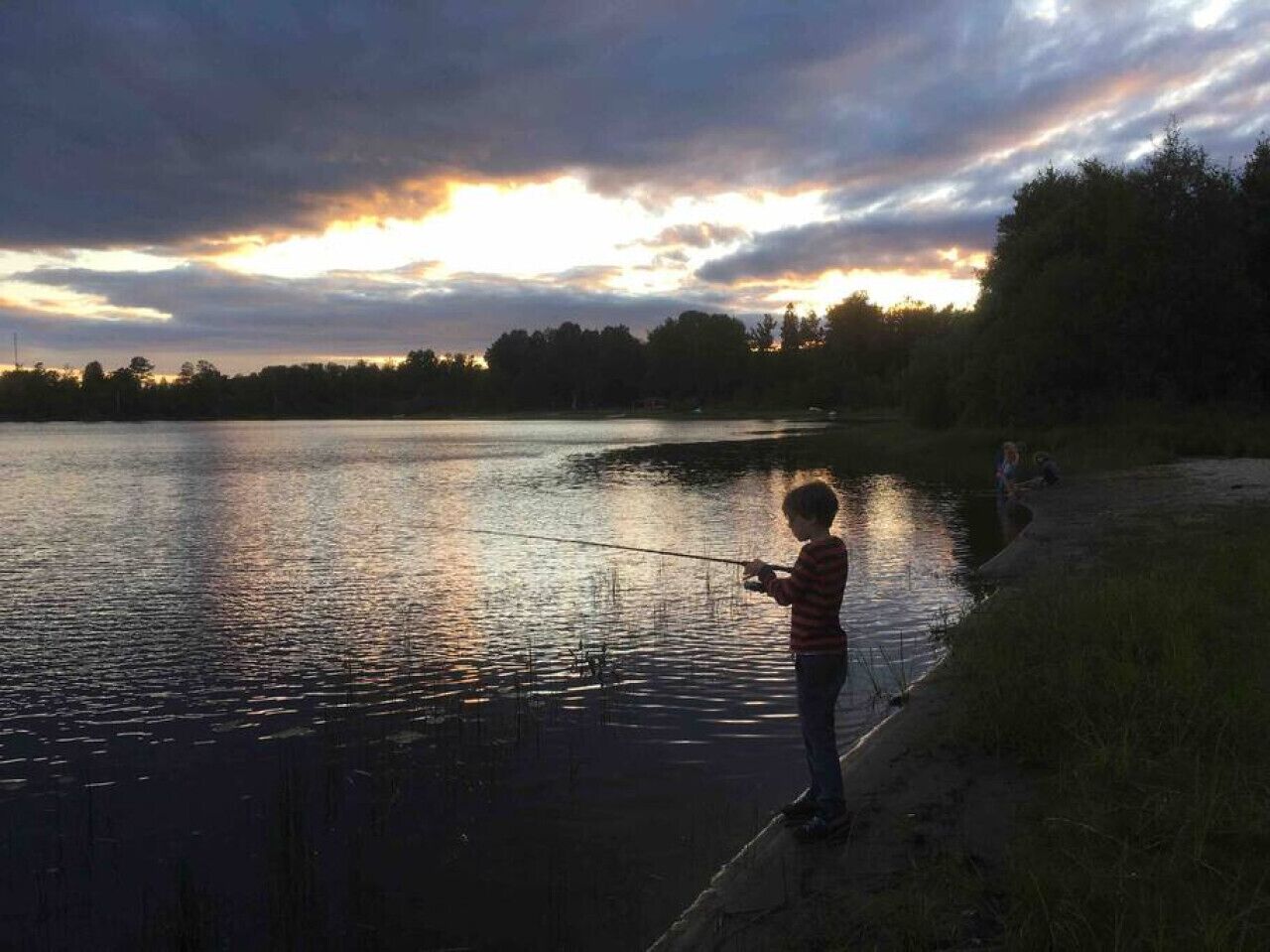 A person fishing by a calm body of water during sunset.