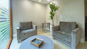 Uma sala de estar moderna com dois sofás cinza, uma pequena mesa de centro redonda e um vaso com planta.
