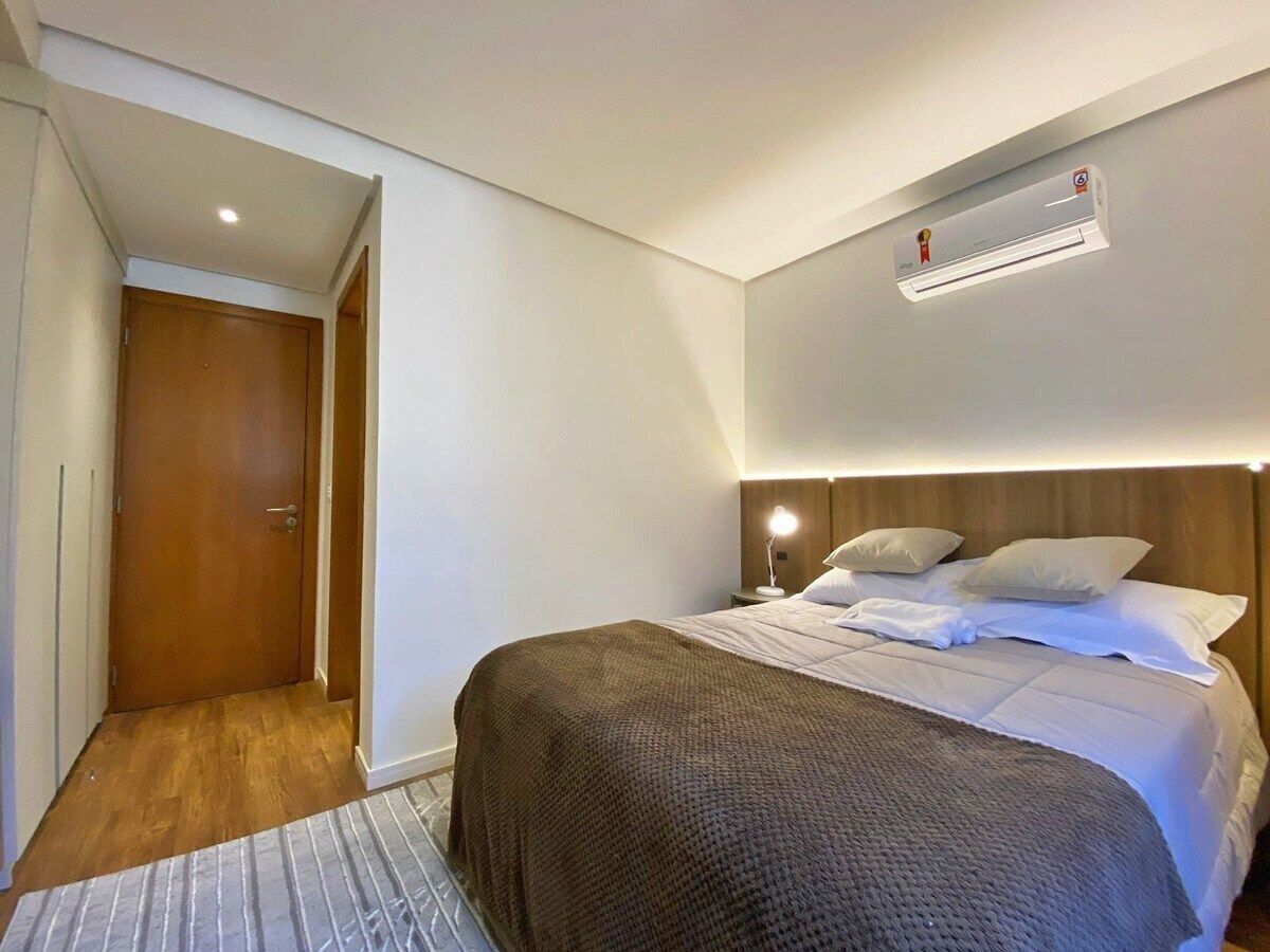 Une chambre à coucher comprenant un lit, une table de chevet, un climatiseur fixé au mur et une porte en bois.