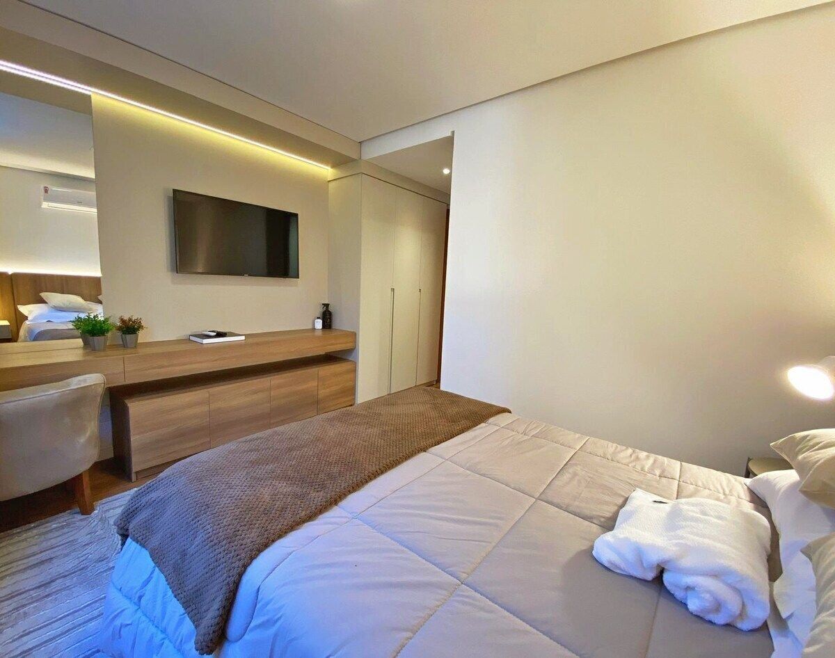 A modern hotel room with a bed, bedside table, TV, and a small desk area.