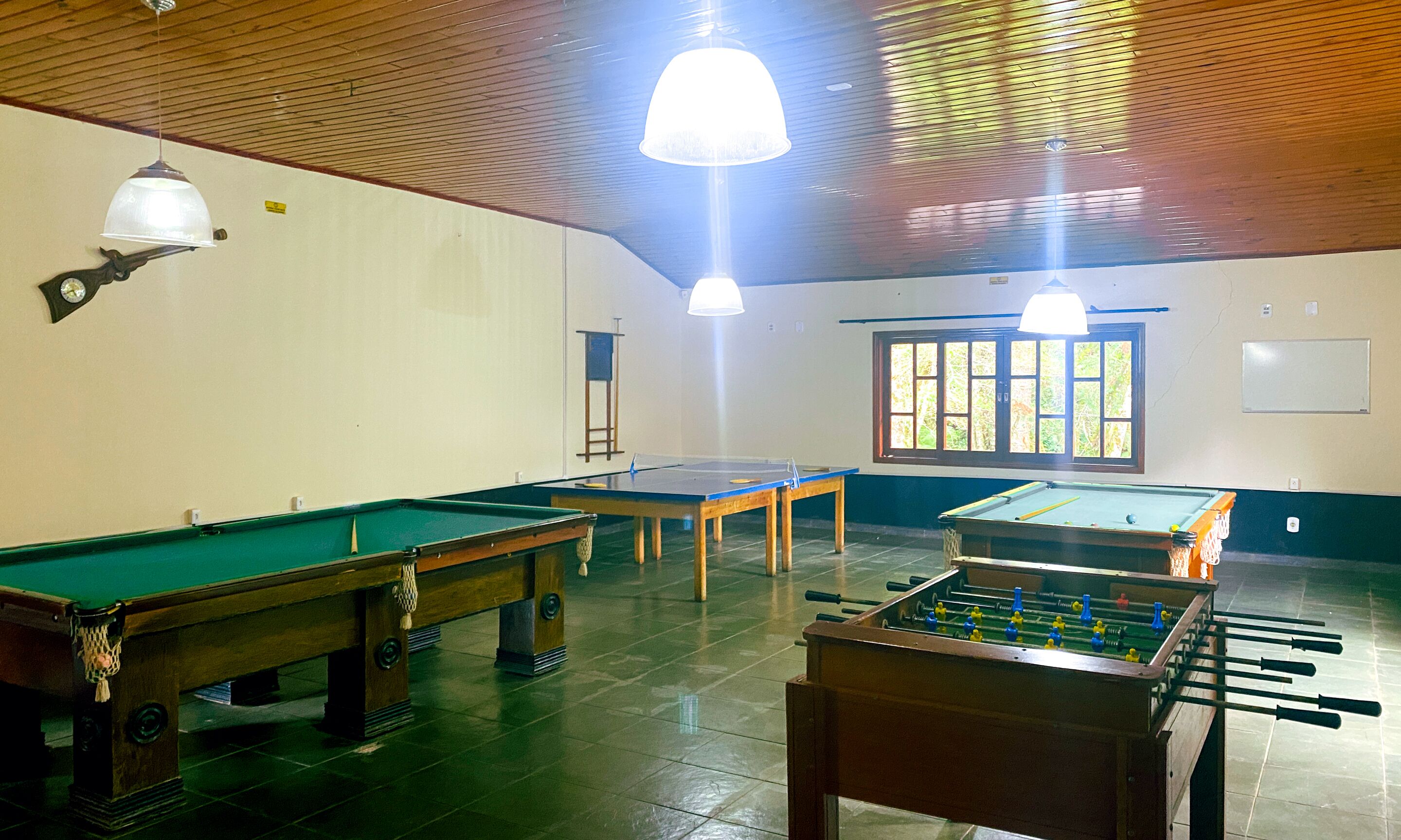 A room with two pool tables, a foosball table, and a window with blinds.
