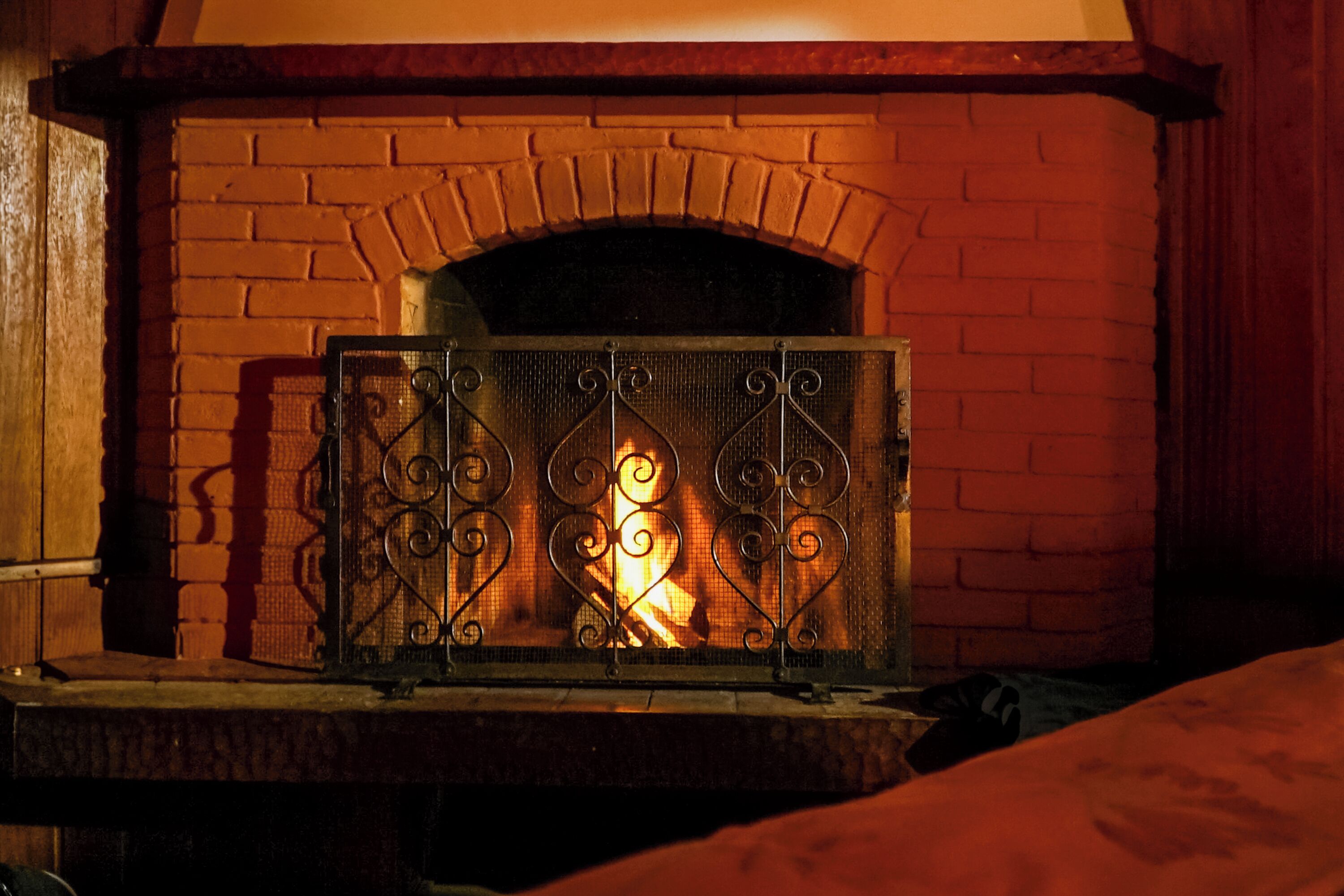 A brick fireplace with a metal screen and a visible fire.