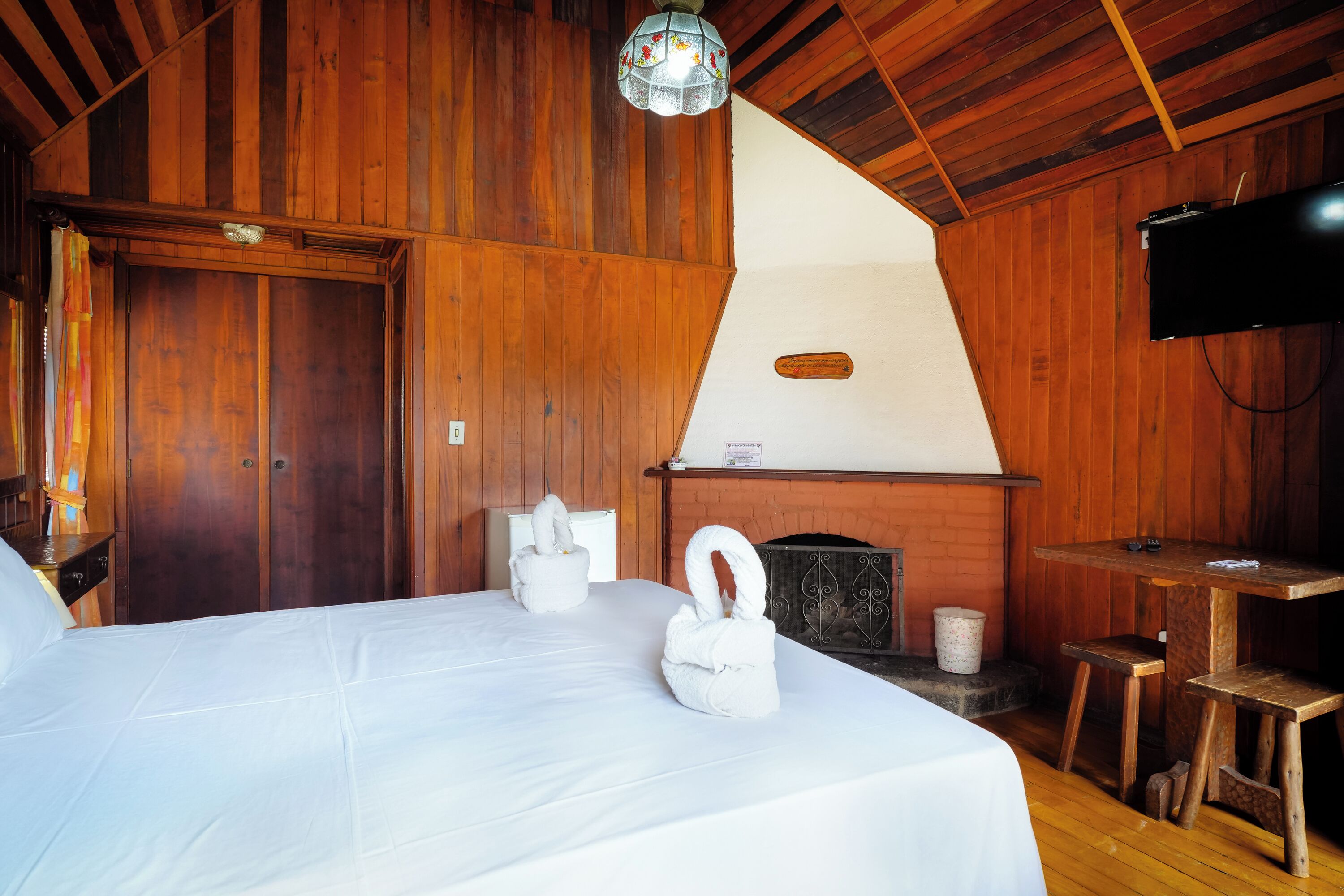 A wooden room with a bed, a fireplace, a television, and a small table.