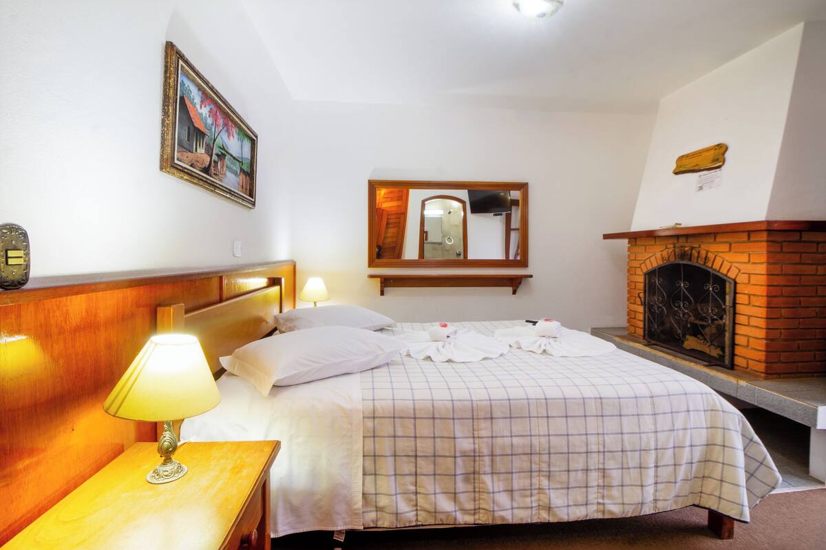Ein Hotelzimmer mit Bett, Nachttisch mit Lampe, Kamin und Spiegel an der Wand.