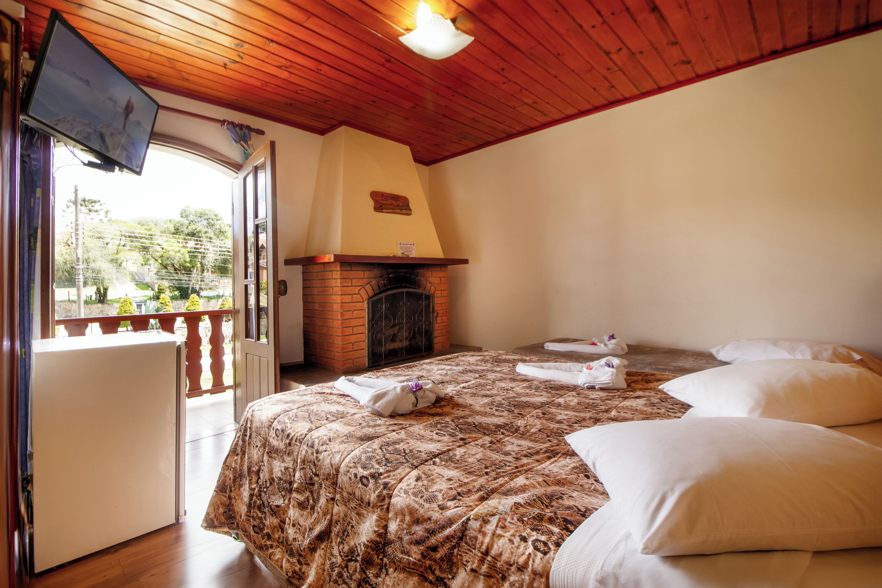 Habitación de hotel con cama, chimenea, televisión y balcón con vistas a zonas verdes.