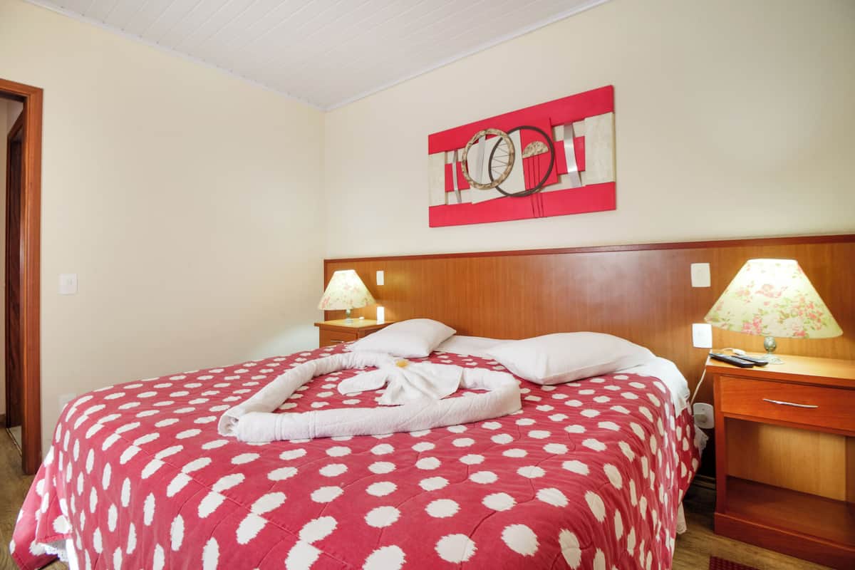Ein Hotelzimmer mit einem Bett, zwei Nachttischen, einem Wandbild und einer rot-weißen Punktebetttdecke.