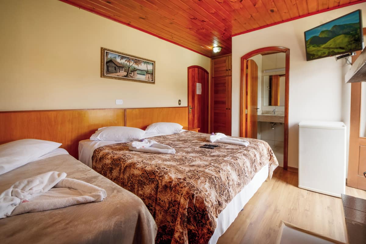Ein Hotelzimmer mit Holzboden, einem Bett mit gemustertem Überwurf, einem kleinen Kühlschrank und einem Gemälde an der Wand.
