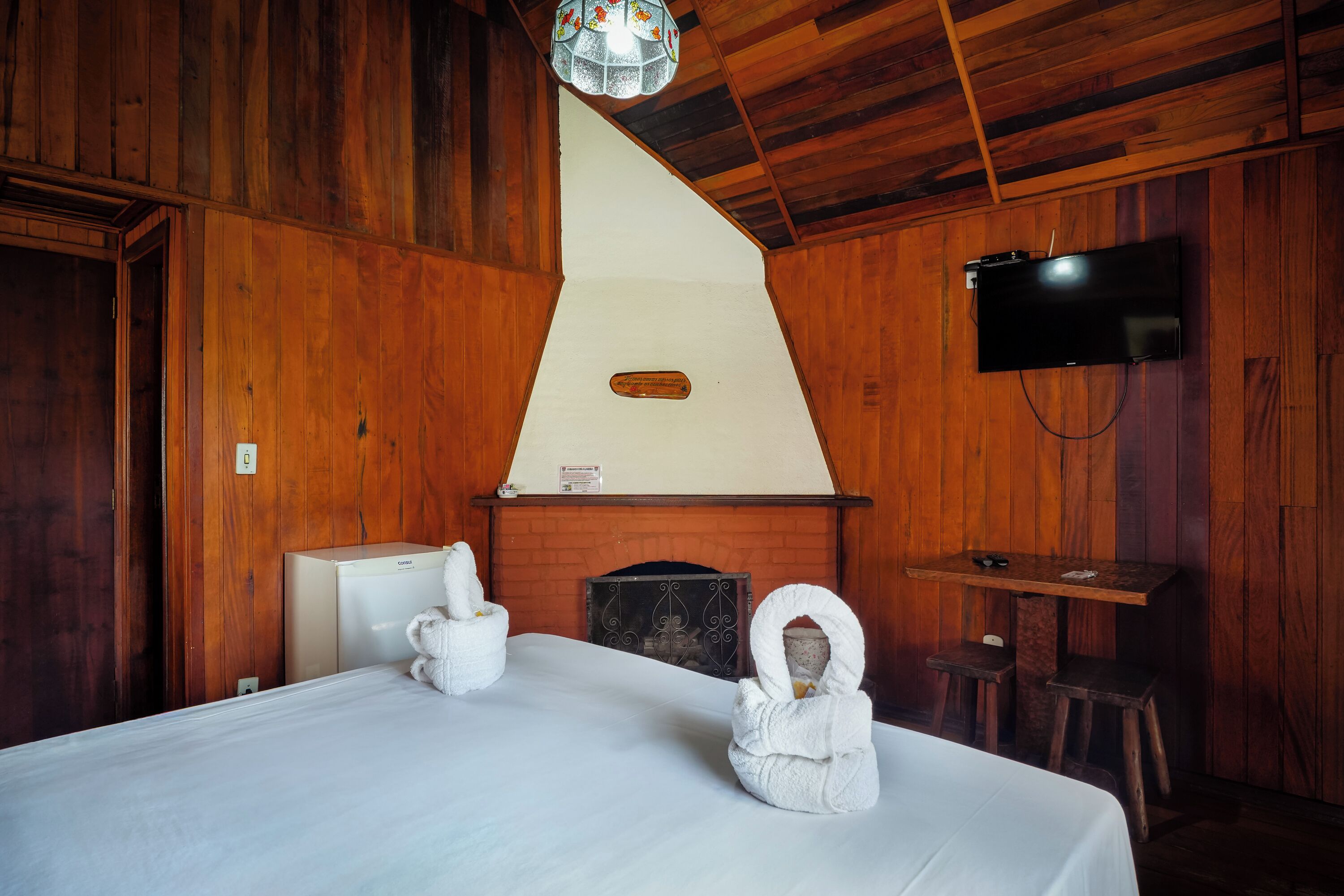 A wooden room with a bed, a television, and a fireplace.