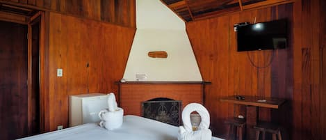 A wooden room with a bed, a television, and a fireplace.