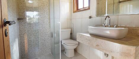 Un baño con ducha, inodoro, lavamanos y ventana.