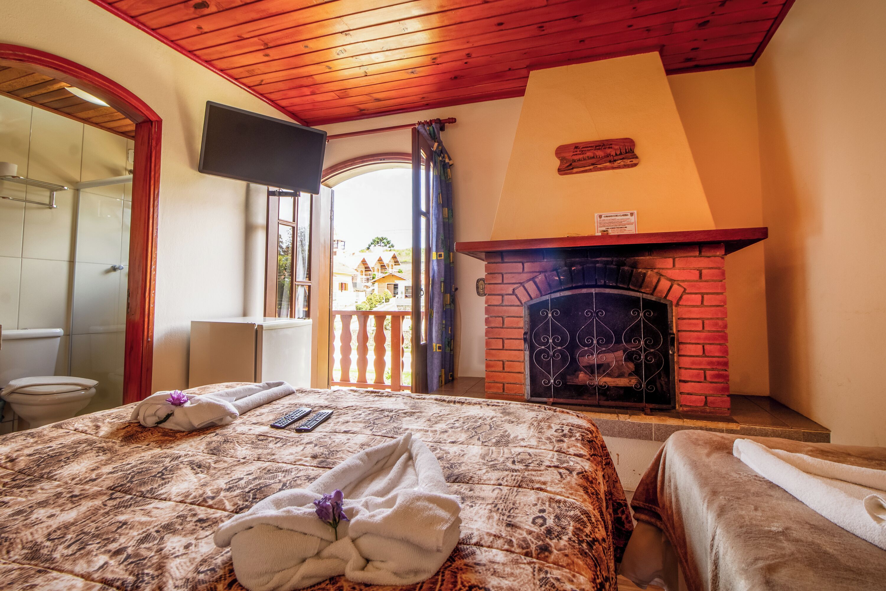 Habitación de hotel con cama, chimenea, televisor en la pared y vista al exterior.