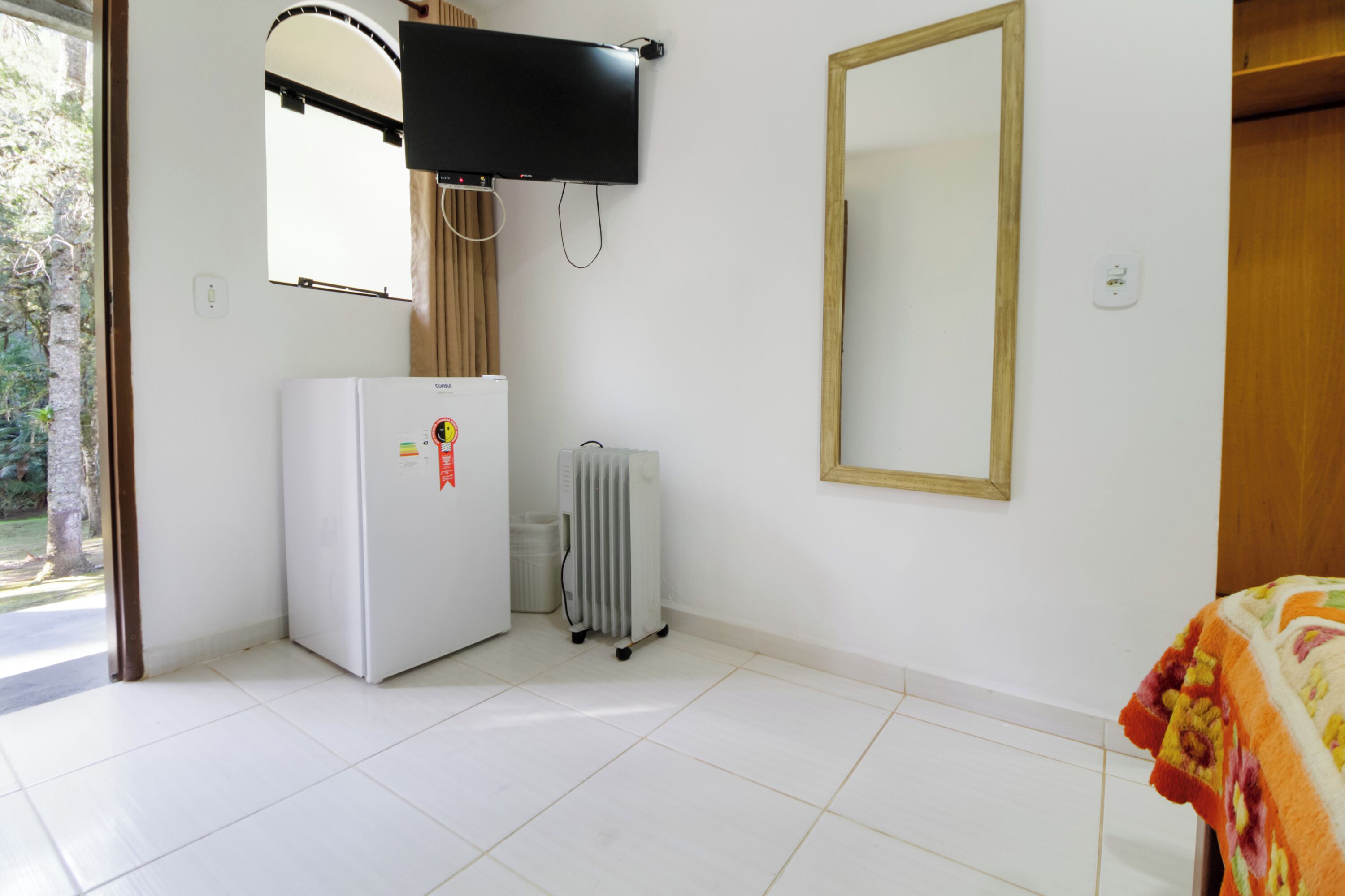 Una habitación con un refrigerador blanco, un televisor montado en la pared, un radiador y un espejo grande.