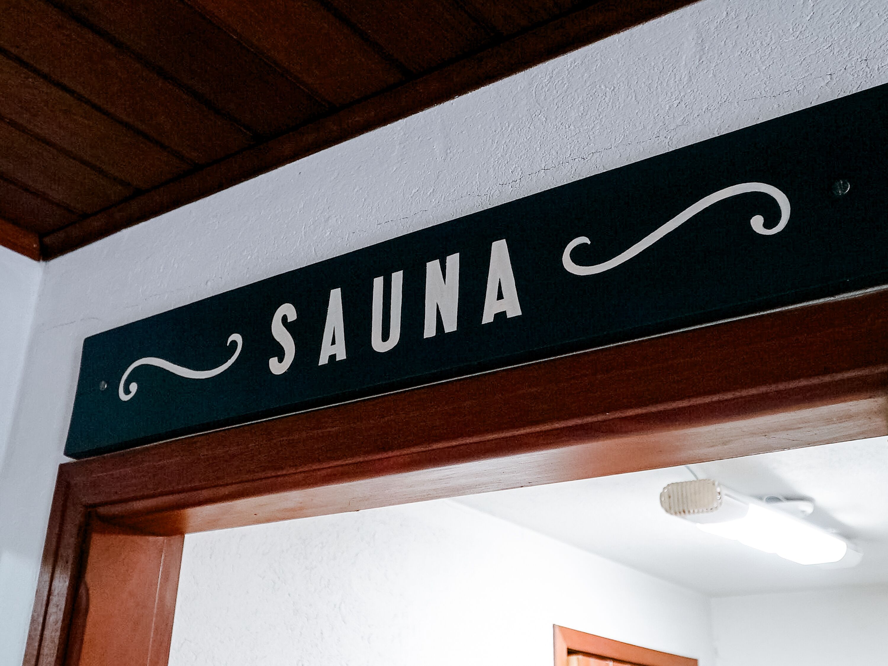 A sign labeled "SAUNA" mounted on a wooden beam above a doorway.