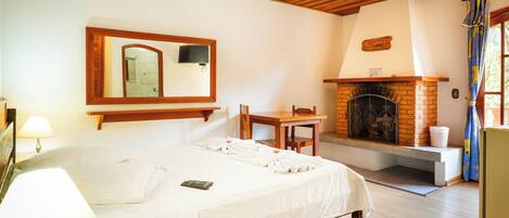 Una habitación de hotel con una cama, techo de madera, chimenea, espejo y televisor.