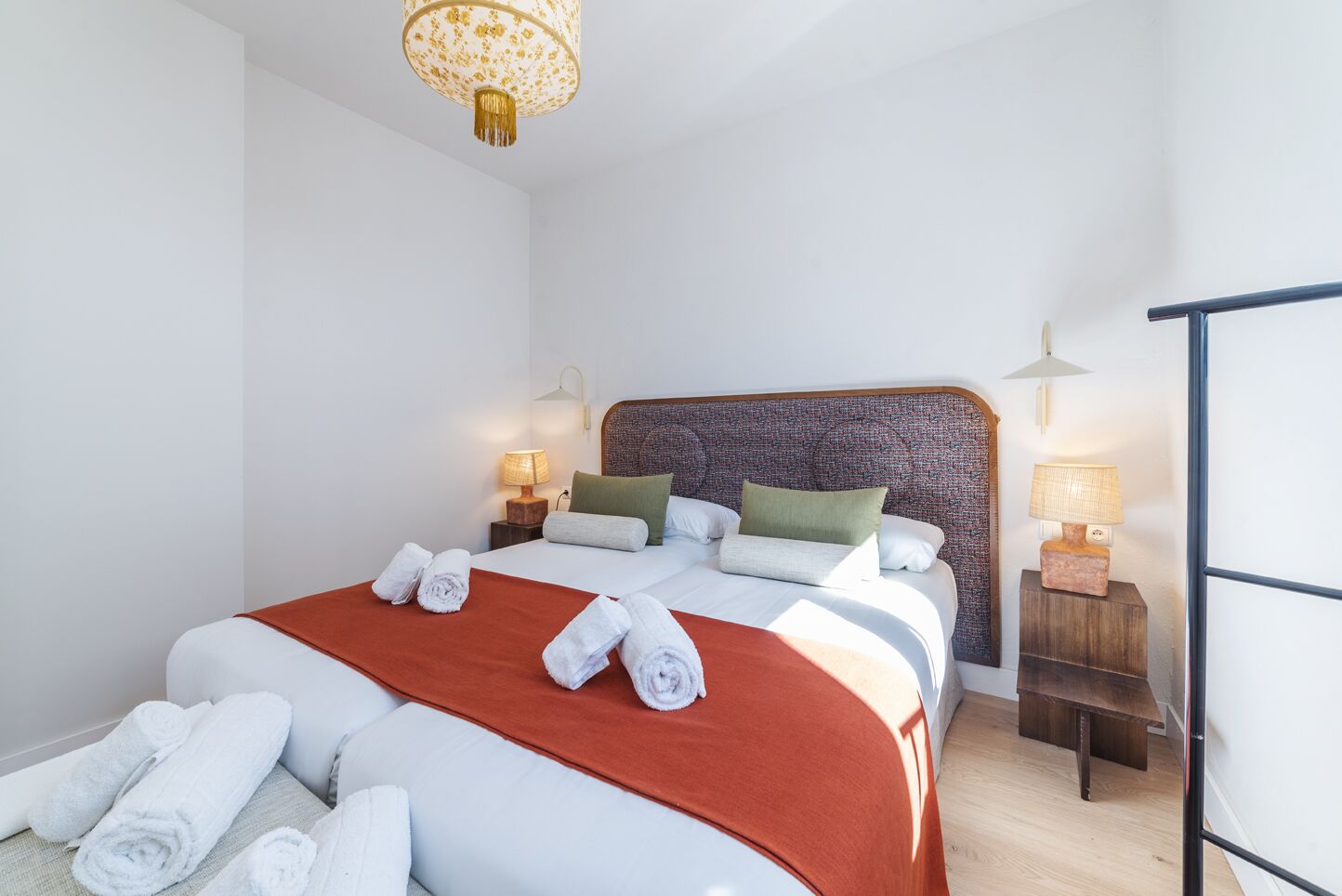 A neatly made bed with rolled towels, two bedside lamps, and a patterned headboard.